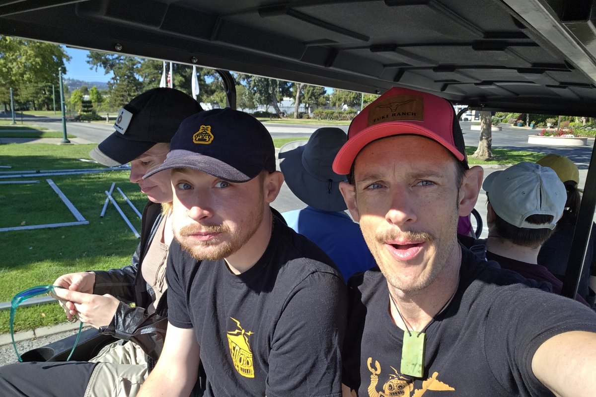Terence Carr and another volunteer in Open Sauce shirts, riding a cart across the event grounds at Open Sauce 2026.